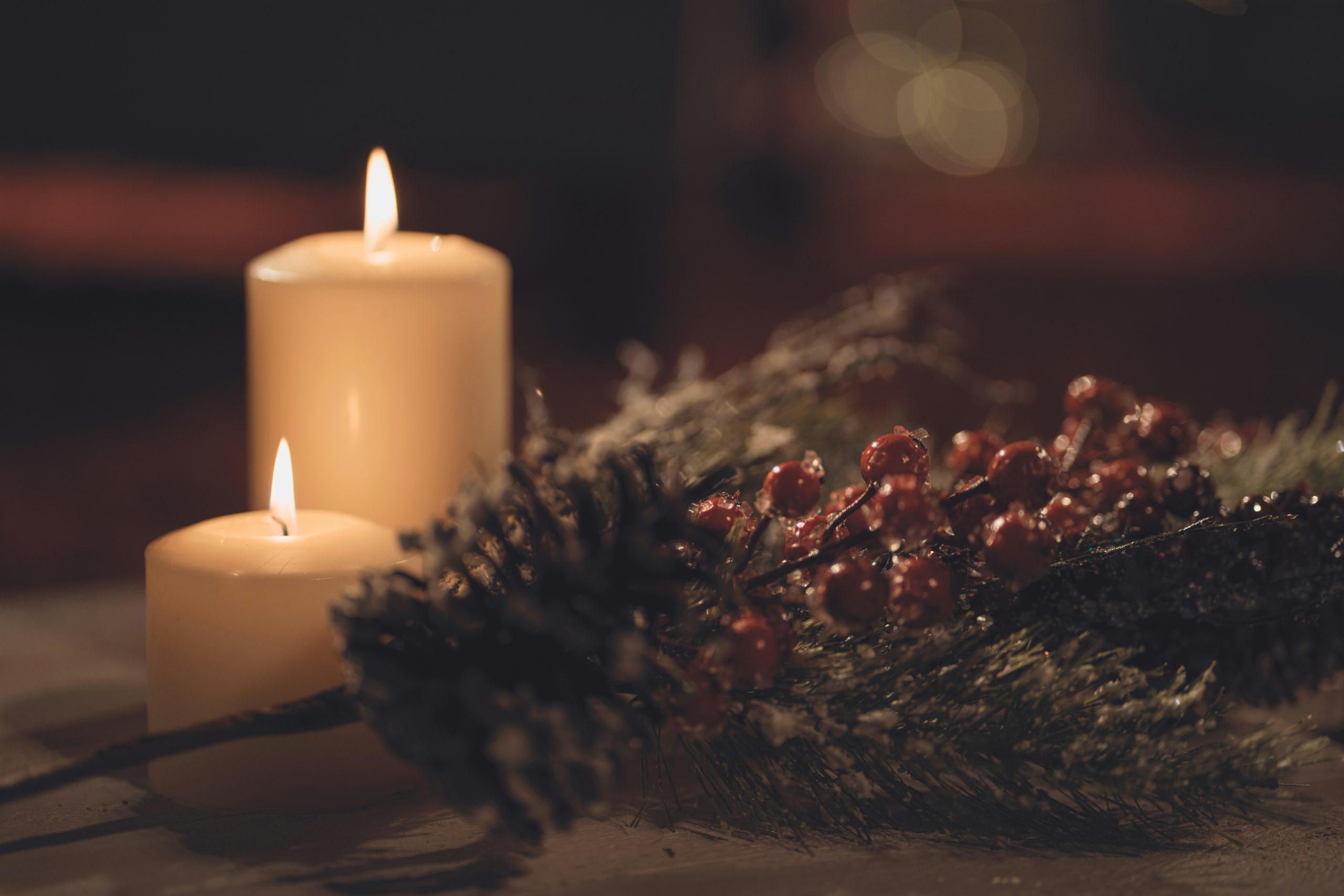 Lit Christmas candles beside a festive wreath with pine cones and red berries